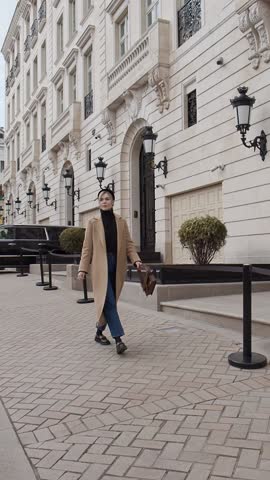 Full length woman walking at historic street of city, against beautiful architecture building, dressed in spring or autumn clothes cashmere beige coat, jeans, turtleneck. Female street style fashion Royalty-Free Stock Footage #3456669863