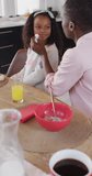 Vertical video of african american mother wiping face of smiling daughter at family breakfast table. Family, domestic life and togetherness concept digitally generated video.
