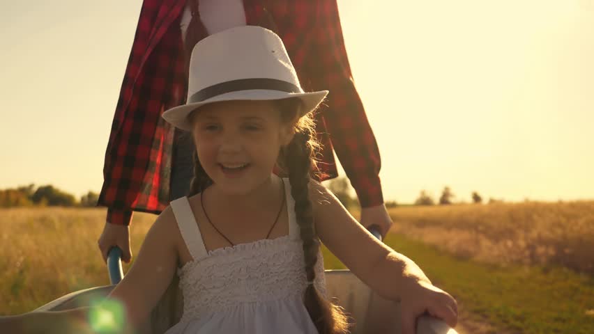 Happy children play in the garden. A little girl is sitting in a garden cart with a hat on. A child rides in a wheelbarrow. Children help to harvest. Happy children of a farmer