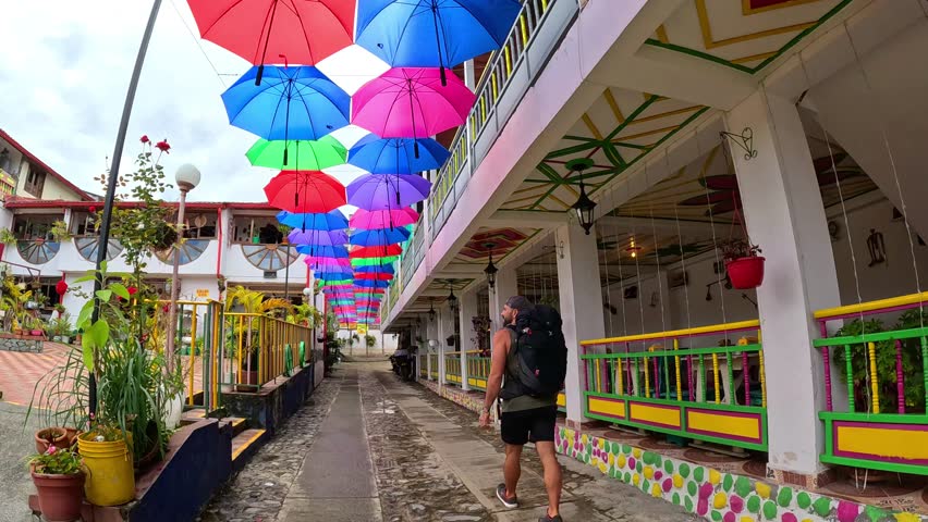A man walking under umbrellas of lots of colours in the street in Salento, Colombia, with a backpack