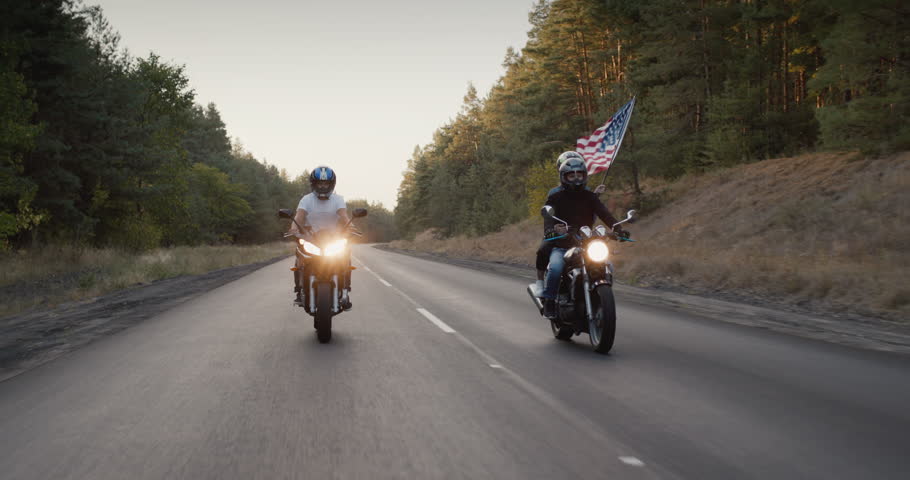 Young people on high-speed motorcycles ride on the highway, a girl holds the U.S. flag. Follow shot