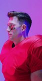 Vertical video of caucasian male american football player wearing helmet, with neon purple lighting. Sport, movement, training and active lifestyle concept.