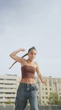 Vertical video of a young woman in stylish clothes dancing in an urban setting in the city.