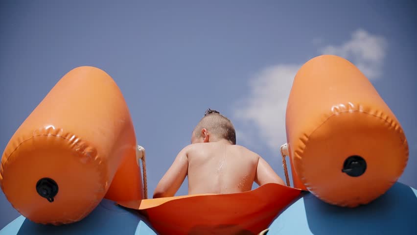 A young boy child waving his hand from the top of a water slide at the Aquapark playground. Summer vacation concept