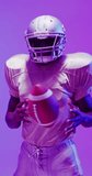 Vertical video of african american male american football player with neon purple lighting. Sport, movement, training and active lifestyle concept.