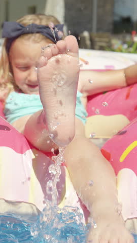 CLOSE UP: Adorable girl floating in pool on inflatable donut and splashing water. Cheerful kid enjoying while having fun in home swimming pool. Outdoor family activities for hot sunny summer days.