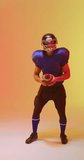 Vertical video of caucasian male american football player holding ball, with neon orange lighting. Sport, movement, training and active lifestyle concept.