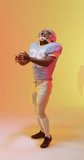 Vertical video of african american male american football player with neon orange lighting. Sport, movement, training and active lifestyle concept.
