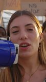 Vertical HD video. Large group of diverse people manifesting against war or attack on a country. Female activist using megaphone outdoors. Stop war signs and banners in a peace demonstration