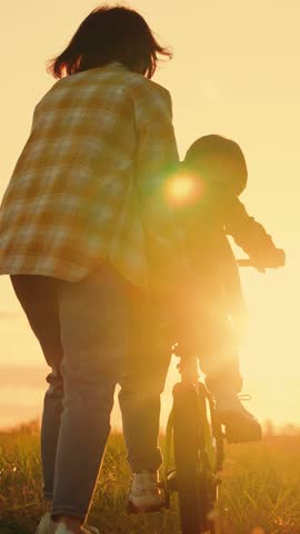 Mother little son learn to ride bike together in summer. Boy, his mother learn to ride bicycle in meadow in sun. Teamwork. Mom teaches her son to ride bike in park at sunset. Family day out in nature Royalty-Free Stock Footage #3456849205
