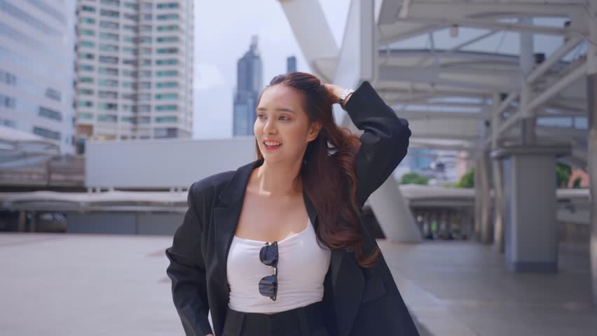 Asian youg beautiful businesswoman walking outdoors in modern city. Attractive employee girl worker feel happy and confident walking around outside the office. Job application and recruitment concept.
