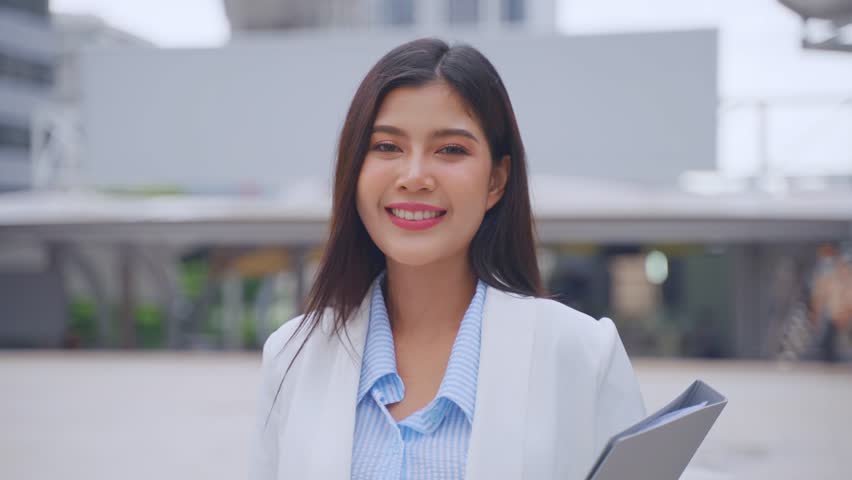 Portrait of Asian youg beautiful businesswoman standing outdoor in city. Attractive employee girl worker feel happy and confident then smile, looking at camera. Job application and recruitment concept