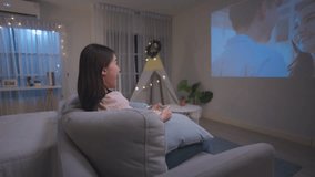 Asian young beautiful woman watch romantic movie on television at home. Attractive casual girl feel happy and relax, sit on sofa having fun watching lovely video on TV show. Activity lifestyle concept