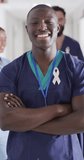 Vertical video of portrait of happy african american male doctor with cancer ribbon. Global medicine, health, lifestyle and hospital concept.
