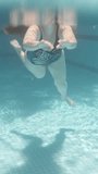 Blue swimming pool, underwater shooting, sunny day. A plump young woman swims in a closed swimsuit Vertical video.
