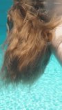 Blue swimming pool, underwater shooting, sunny day. The young woman lies on her back, Long hair sways under the water Vertical video.