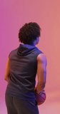 Vertical video of biracial male basketball player throwing ball on pink background. Sports and competition concept.