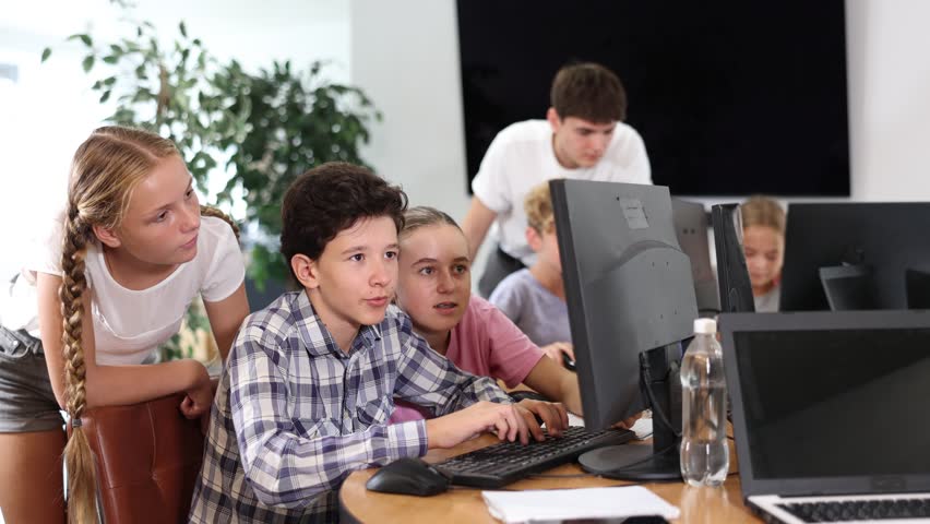 Curious underage boys and girls looking at monitor of computer together with trainer during IT courses Royalty-Free Stock Footage #3456953171