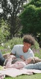 Vertical video of happy diverse couple having picnic in garden on sunny day. Spending quality time at home concept.