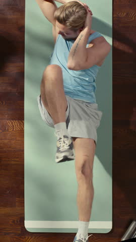Vertical Screen Top View Sport: Gorgeous Guy Doing ABS Elbow to Knee Crunches Lying on an Exericise Mat at Home. Muscular, Fit, Really Handsome Athletic Man Does Workout in His Apartment. Above Shot
