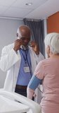 Vertical video of african american male doctor examining senior caucasian female patient at hospital. Medicine, healthcare, lifestyle and hospital concept.