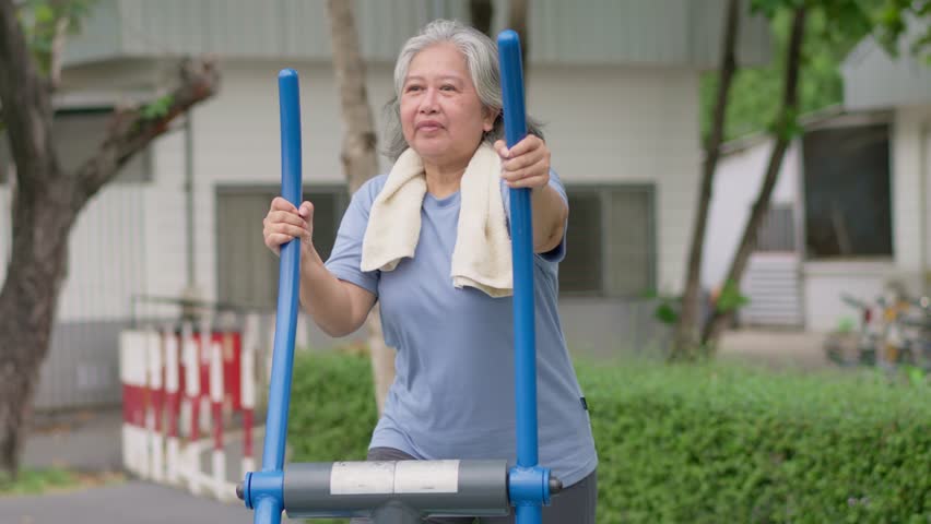 Senior Asian woman in casual workout in exercise stations in public park. Represents keeping young with physical activity, Open air gym. Physical health concept. Outdoor fitness equipment in city park Royalty-Free Stock Footage #3457043251