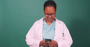 Young Black female doctor works on cellphone, smiles at the camera