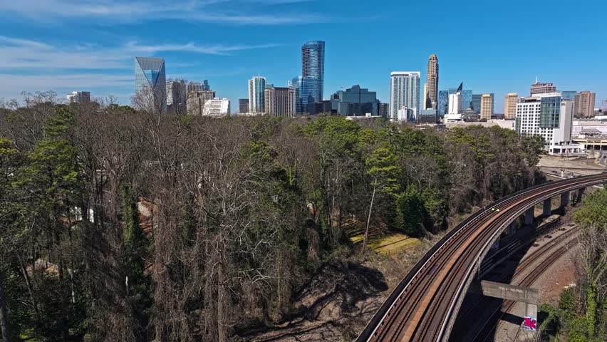 High Rails in suburb forest of Atlanta Town in sunlight. Skyline with Skyscraper buildings in background. Blue sky in summer. Rising drone wide shot.
