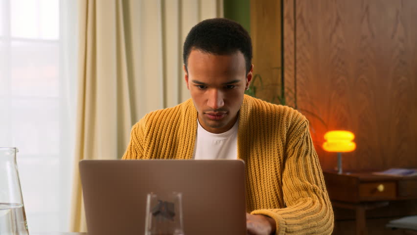 portrait of young Latin man sitting at table working at laptop at home, looks in camera nodding head and smiling in sign of assenting and success. contented and pleased student of online education - Powered by Shutterstock - Get 15% off with code: PIKWIZARD15