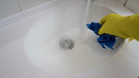 Cleaning a white ceramic sink in a bathroom close-up. A woman wearing yellow gloves washes the sink with disinfectants during home cleaning. - Powered by Shutterstock - Get 15% off with code: PIKWIZARD15