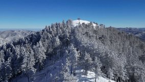 Aerial drone view of mountain peak surrounded by frozen trees. Mountain landscape on a sunny winter day.