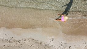A woman in a pink swimsuit and straw hat walks along a sandy beach. Top-down perspective. - Powered by Shutterstock - Get 15% off with code: PIKWIZARD15