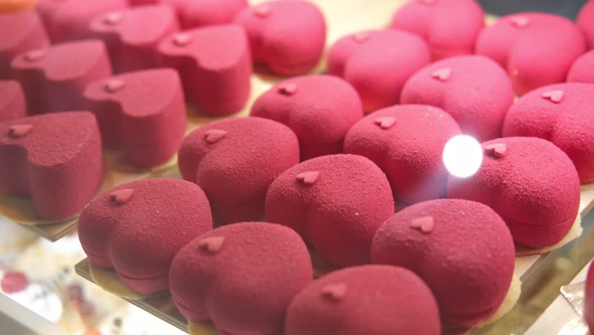 Delicious heart shaped red cakes pastries on a display showcase of coffee shop, bakery or cafe. Confectionery counter with sweet tasty desserts. Candy, patisserie. Valentine