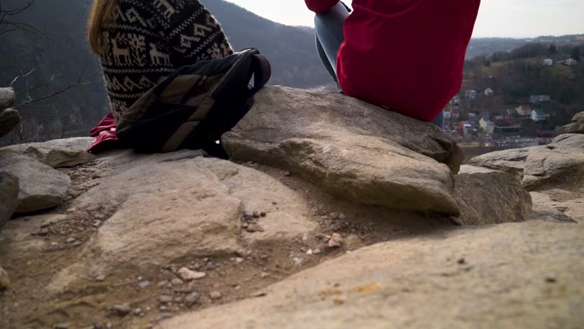 Camera booms up from rocks to reveal mature blonde mother and son talking at an overlook of Harpers Ferry National Park.