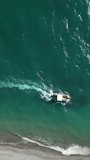 Aerial video of a white boat with tourists rides on the sea near pebble beach. Vertical video.