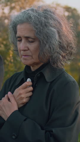 Side vertical footage of Caucasian senior lady praying and crying during memorial ceremony at cemetery