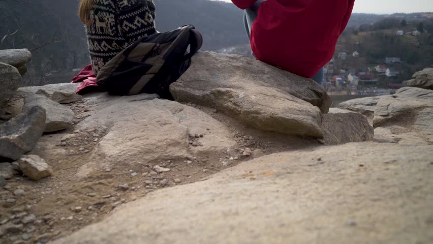 Camera booms up from rocks to reveal mature blonde mother and son talking at an overlook of Harpers Ferry National Park.