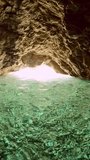 Vertical video, POV underwater shot, man dives underwater and swims out from cave, Slow motion. First person view, Close up of hands man swimming underwater in cave