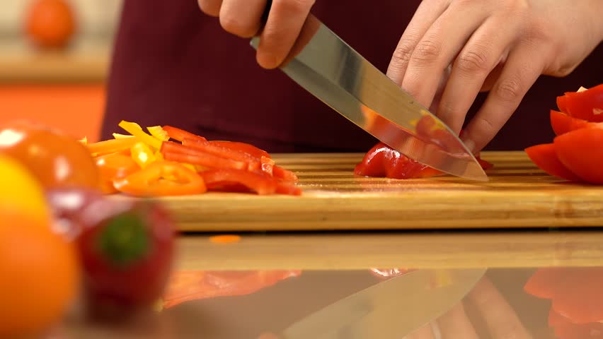 Cutting red bell pepper in dices with knife. Chef's hand chopped bell pepper on cutting, wooden board. Vegetable salad. Man cutting a slice of red paprika. Healthy Food.