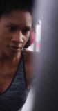 Vertical video of determined african american woman boxing training with punchbag at gym. Exercise, fitness and healthy lifestyle.