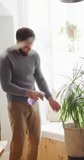 Vertical video of happy caucasian man watering houseplants at home, copy space. Happiness, free time, ecology, togetherness and domestic life.