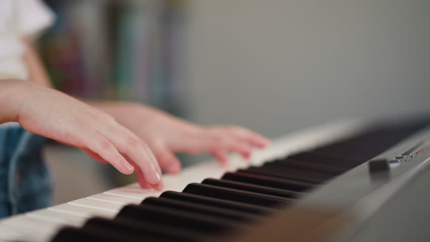 Girl hands press keys on keyboard of musical instrument. Child performs expressive melody on synthesizer. Little musician practices at home closeup on blurred background