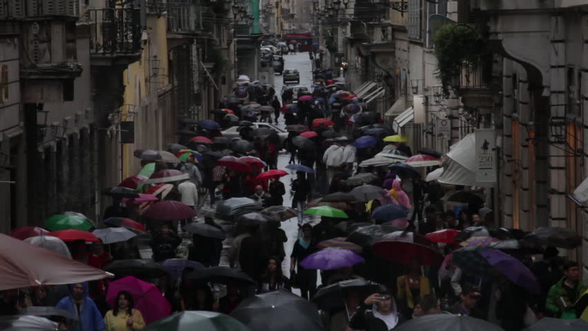 Hundreds of tourists holding umbrellas walking down Via dei Condotti