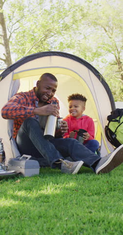 Vertical video of african american man and his son sitting in tent in garden. Spending quality time at home.