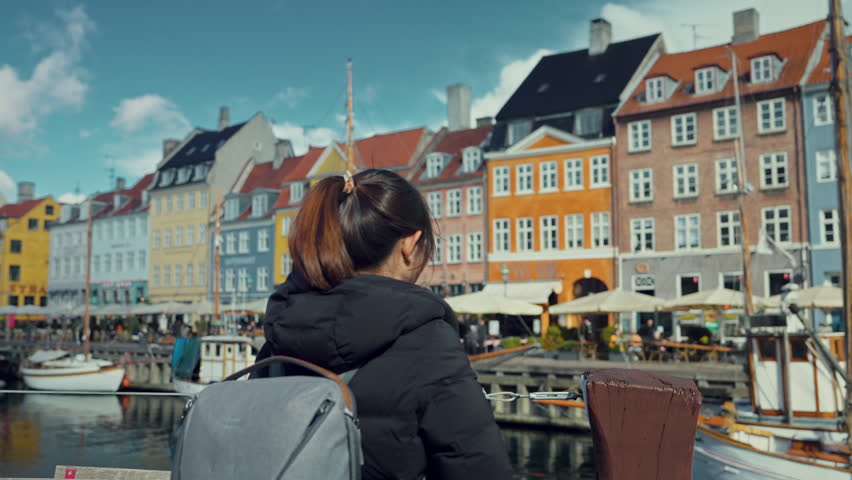 Asian tourist woman backpacker traveler with her camera at Copenhagen Nyhavn, Famous landmark, northern Europe destination, the old town waterfront water canal in the capital Kobenhavn in Denmark.