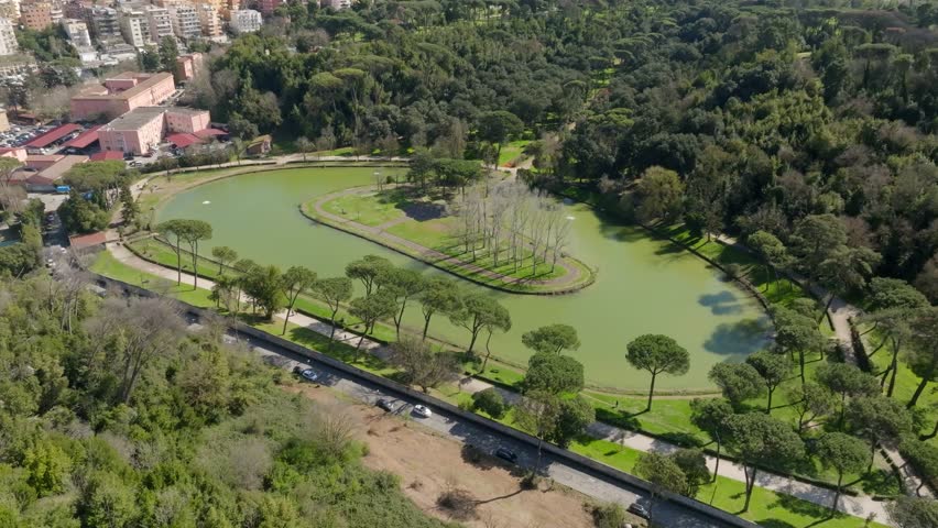 Aerial view of the small lake of Villa Ada, a public park in Rome, Italy. In the center of the lake there is a small island with trees and a green area. Royalty-Free Stock Footage #3457459219