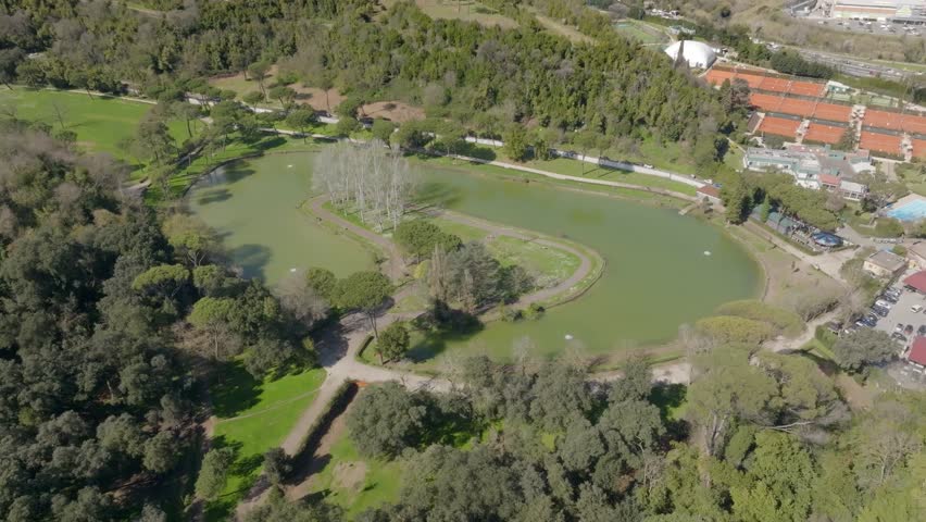 Aerial view of the small lake of Villa Ada, a public park in Rome, Italy. In the center of the lake there is a small island with trees and a green area. Royalty-Free Stock Footage #3457459517