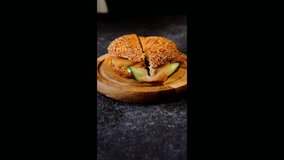 Step-by-step preparation of a sandwich, bagel with salted salmon, cucumber and cream cheese. Showing a cutaway view of the finished sandwich on a wooden board. Video recipes. Sandwiches recipes