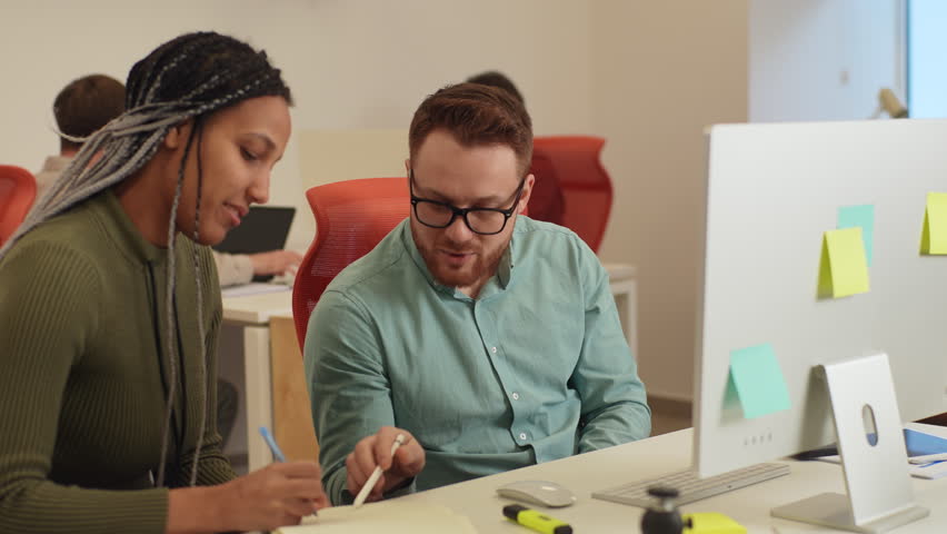 Professional male teacher, manager or mentor helping African-American student, new employee, teaching intern, explaining online job using laptop computer, talking, having teamwork discussion in office