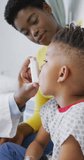 Vertical video of african american male doctor examining child patient at hospital. Medicine, healthcare, lifestyle and hospital concept.